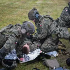 Żołnierze udzielają pomocy rannemu koledze na trawie. Kategoria e: szkolenie medyczne w terenie.