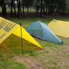 Trzy namioty na trawie. Dwa żółte z napisem "OUTDOOR" i jeden zielony. Namiot z tarpa gotowy na przygodę.