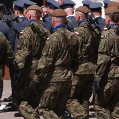 Żołnierze w mundurach polowych maszerują w szyku, każdy z bagnetem na karabinie.