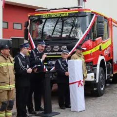 Zastępca naczelnika OSP Tuchomie stoi obok nowego wozu strażackiego, podczas uroczystości.