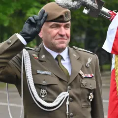 Pułkownik Suliwiński w mundurze salutuje obok polskiej flagi.