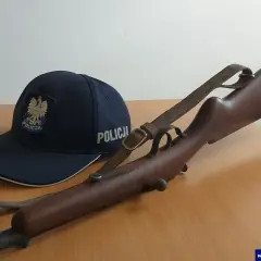 Policyjna czapka i karabin, prawdopodobnie kbks bez pozwolenia, leżą na drewnianym stole.