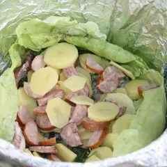 Gotowe dania na ognisko: ziemniaki, kiełbasa i kapusta zawinięte w folię aluminiową, czekają na pieczenie.