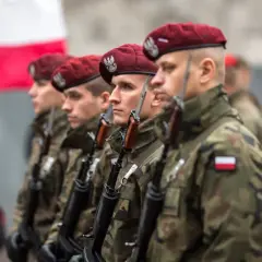Żołnierze w bordowych beretach i mundurach moro, z karabinami, stoją w szeregu. W tle polska flaga. To dumne kategorie wojskowe.