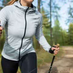 Kobieta z kijkami nordic walking w lesie. Dowiedz się, jak dobrać odpowiednie kijki do swojego wzrostu i stylu marszu.