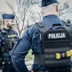 Dwóch policjantów w mundurach i kamizelkach taktycznych. Widoczne wyposażenie policjanta: radiostacja, kabura na broń, pas z ładownicami.