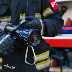 Aspirant straży pożarnej w rękawicach trzyma prądownicę.