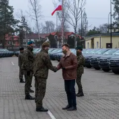 Rangers wojsko odbierają nowe pojazdy. W tle rzędy samochodów i polska flaga.