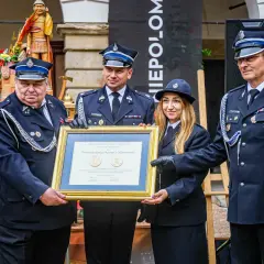 Członkowie OSP otrzymują odznaczenie. W tle drewniana figura i baner.