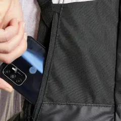 Dłoń wkłada telefon do bocznej kieszeni czarnego plecaka. Idealny, jaki plecak na rower, by mieć wszystko pod ręką.