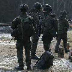 Żołnierze w pełnym rynsztunku, w tym kapitan major, stoją przy torach kolejowych.