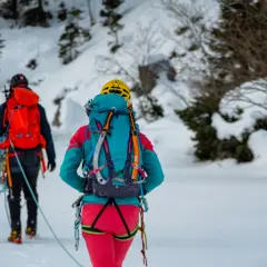 Dwóch alpinistów w zimowych strojach, z plecakami i sprzętem, przemierza ośnieżony teren. To inspiracja, co zabrać w góry zimą.