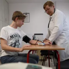 Młody mężczyzna przechodzi badania podczas komisji wojskowej. Lekarka mierzy mu ciśnienie.