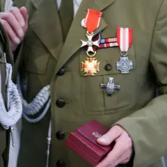 Żołnierz w mundurze z licznymi odznaczeniami wojskowymi na piersi. W dłoni trzyma małe, czerwone pudełko.