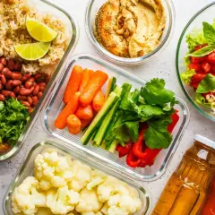 Gotowe pojemniki z jedzeniem na biwak bez gotowania: ryż z fasolą i pieczarkami, warzywa pokrojone w słupki, kalafior, sałatka z pomidorami i awokado, hummus i napoje.