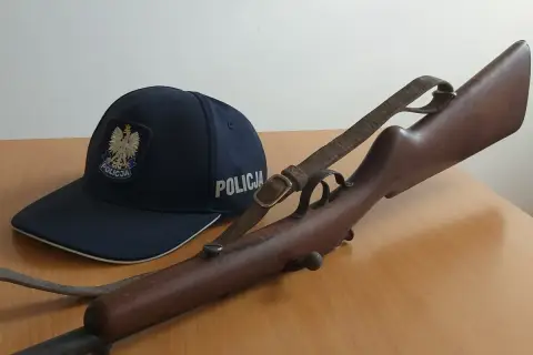 Policyjna czapka i karabin, prawdopodobnie kbks bez pozwolenia, leżą na drewnianym stole.