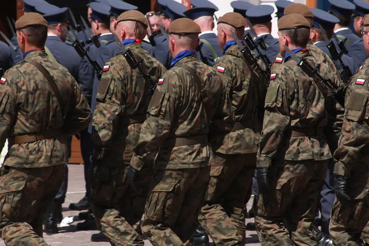 Żołnierze w mundurach polowych maszerują w szyku, każdy z bagnetem na karabinie.