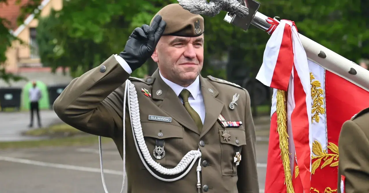 Pułkownik Suliwiński w mundurze salutuje obok polskiej flagi.