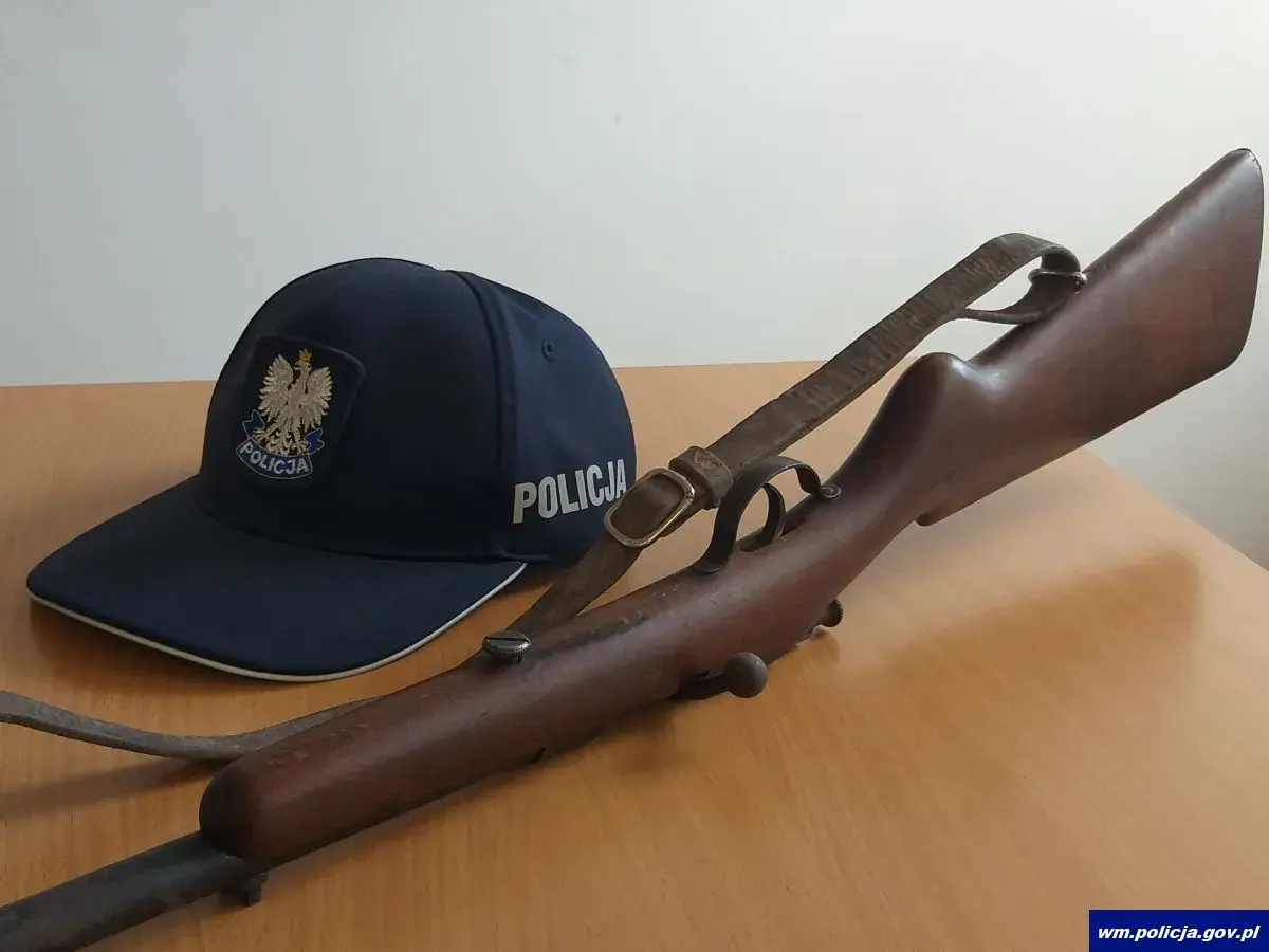 Policyjna czapka i karabin, prawdopodobnie kbks bez pozwolenia, leżą na drewnianym stole.