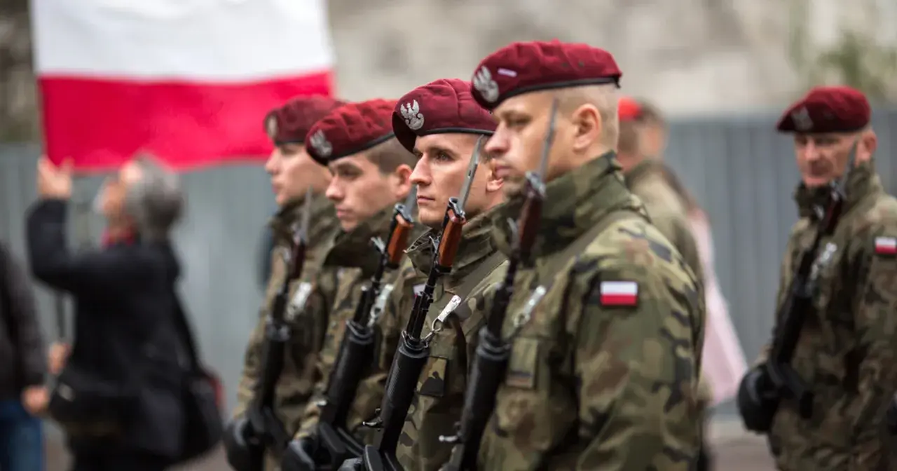 Żołnierze w bordowych beretach i mundurach moro, z karabinami, stoją w szeregu. W tle polska flaga. To dumne kategorie wojskowe.