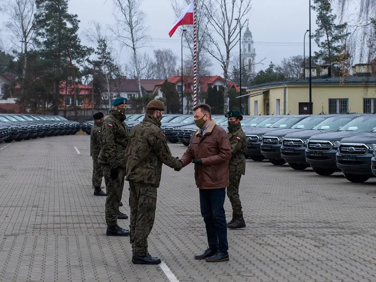 Rangers wojsko odbierają nowe pojazdy. W tle rzędy samochodów i polska flaga.