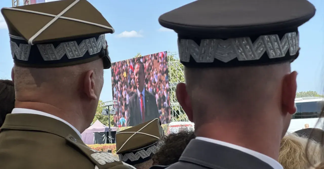Dwóch mężczyzn w mundurach, jeden z nich ma jedną gwiazdkę na pagonie, ogląda przemówienie na telebimie.