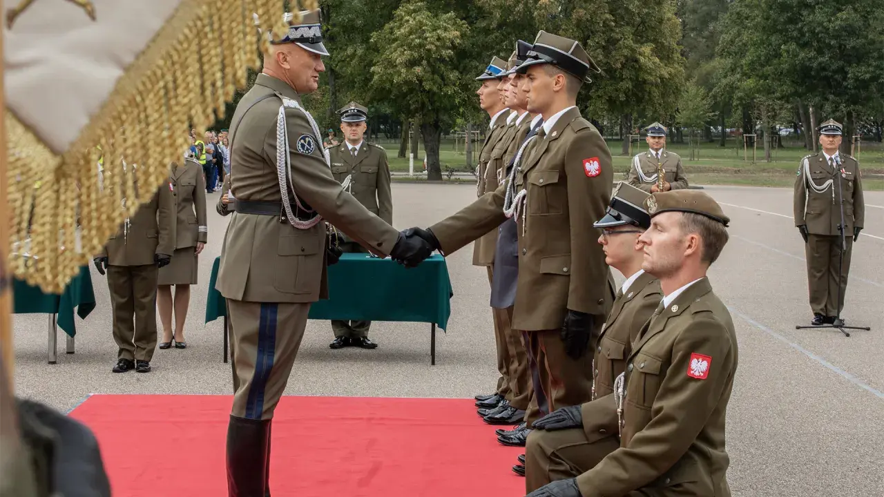 Podporucznik skrót. Uroczystość wręczenia odznaczeń wojskowych. Dwóch oficerów w mundurach ściska sobie dłonie.