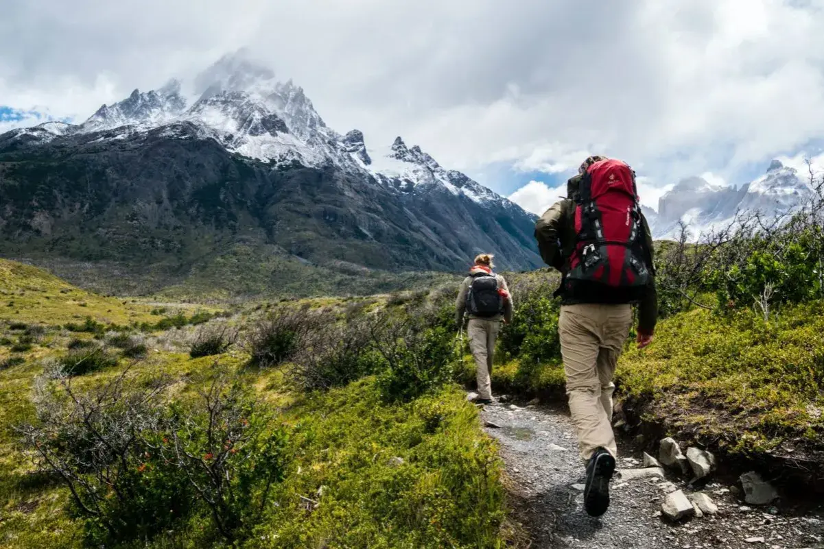 Dwie osoby z plecakami idą ścieżką w górach. To jest właśnie co to trekking – podróżowanie pieszo po trudnym terenie.