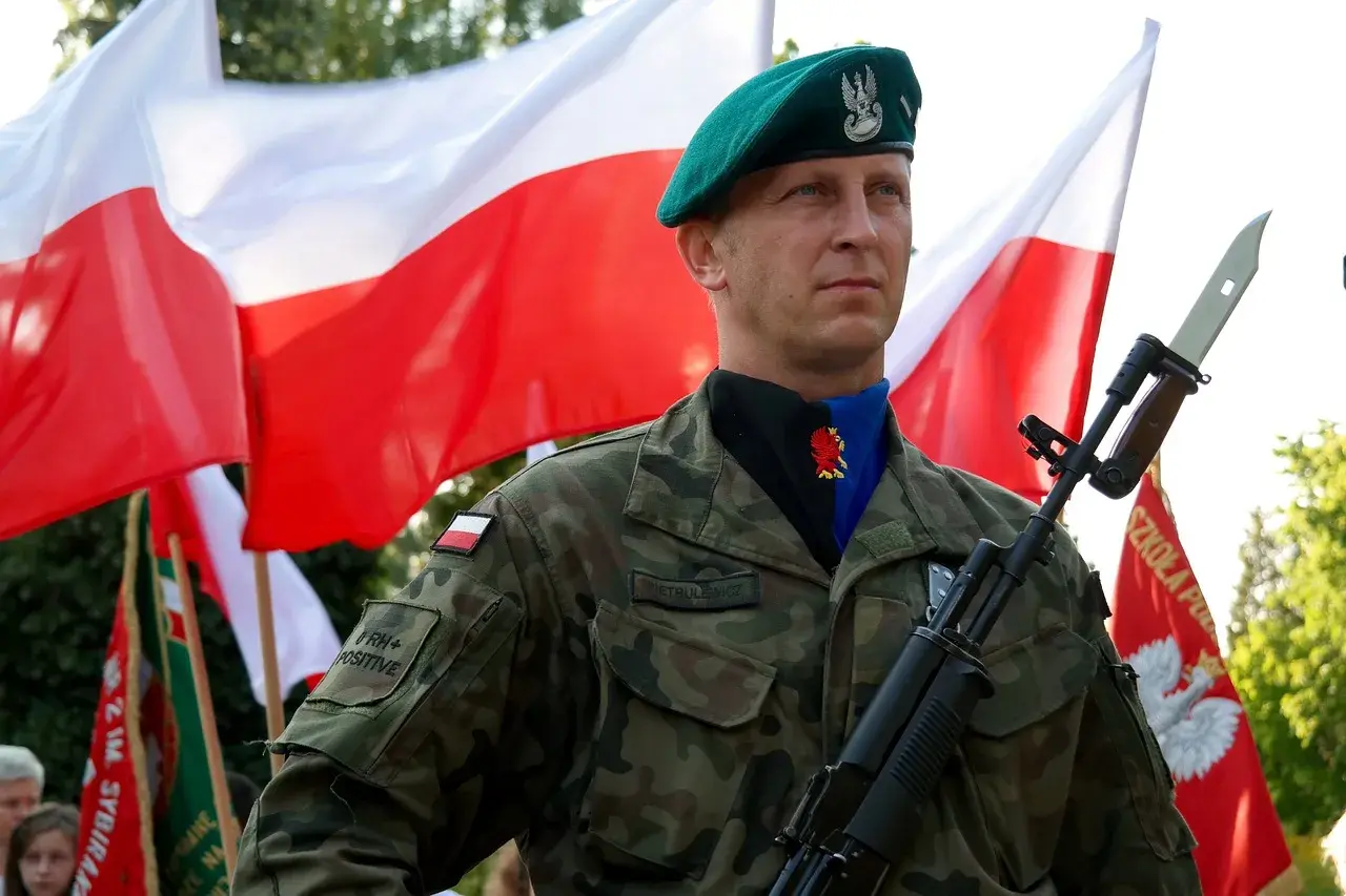 Żołnierz w zielonym berku i mundurze, z karabinem na ramieniu, na tle polskich flag. Widać jego stopnie wojskowe i nazwisko.