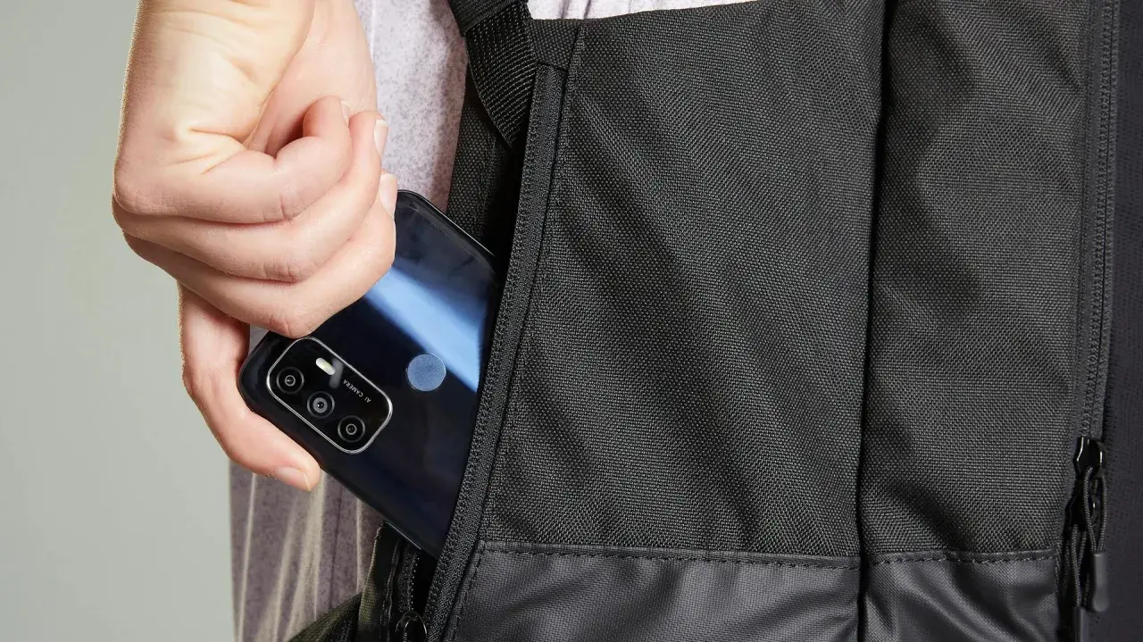 Dłoń wkłada telefon do bocznej kieszeni czarnego plecaka. Idealny, jaki plecak na rower, by mieć wszystko pod ręką.