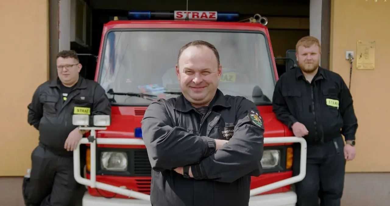 Trzech strażaków OSP pozuje przed wozem strażackim.