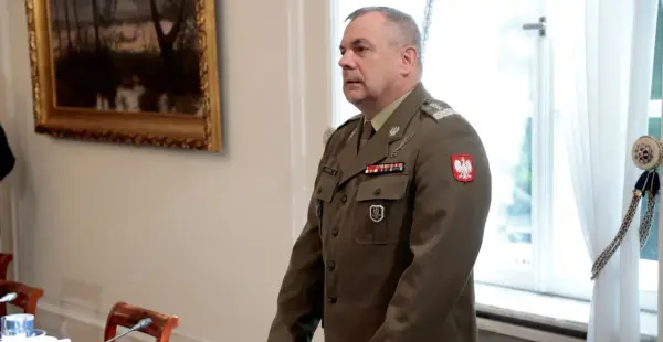 Generał w mundurze, z orłem na piersi, stoi w sali, gdzie odbywa się spotkanie korpusu generałów.